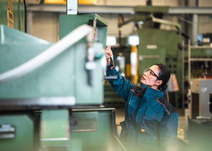 Junge Frau an einer Maschine in der Produktionshalle